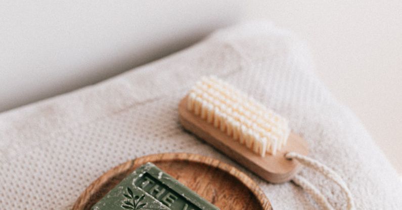 Sustainable Materials - From above composition with natural green soap on eco friendly wooden holder and sustainable brush lying on folded clean soft fresh gray towels against white wall