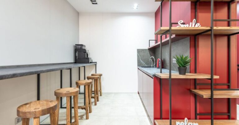 Kitchen Organization - Interior of modern workplace with counter and stools next to open kitchen with cabinets near wooden shelves with potted plant and words relax and smile