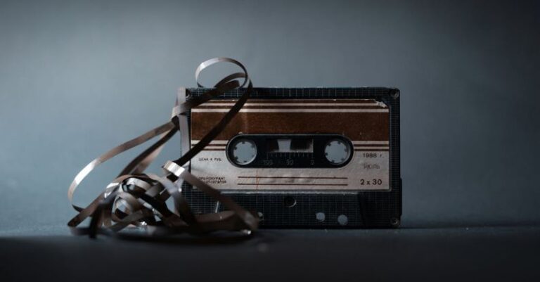 Compact Designs - Retro audio cassette with tape out placed on gray surface and illuminated by light in studio